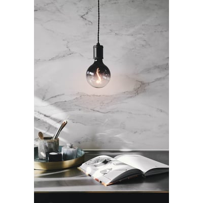 Halo Design COLORS Soft Light LED G125 lampe med røgfarvet glas hænger over et bord med en åben bog og dekorative elementer.