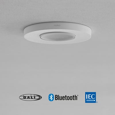 Niko P46MR DALI tilstedeværelsessensor til indbygning i hvid, vist monteret på et lyst loft med DALI, Bluetooth og IEC logoer.