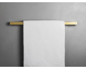 Unidrain Reframe håndklædestang i messing, 60 cm, med et hvidt håndklæde monteret på en grå væg.