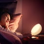 Nærbillede af en kvinde, der slapper af i sengen med en Philips Hue Go lampe, der giver et blødt, varmt hvidt lys.