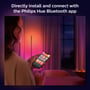 Kvinde holder en smartphone med Philips Hue appen, mens hun styrer en gulvlampe i et rum med farvet lys.