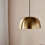 Nordlux Cera pendel i blank messing med en rund skærm, hængende foran en lyserød væg og et hvidt gardin.